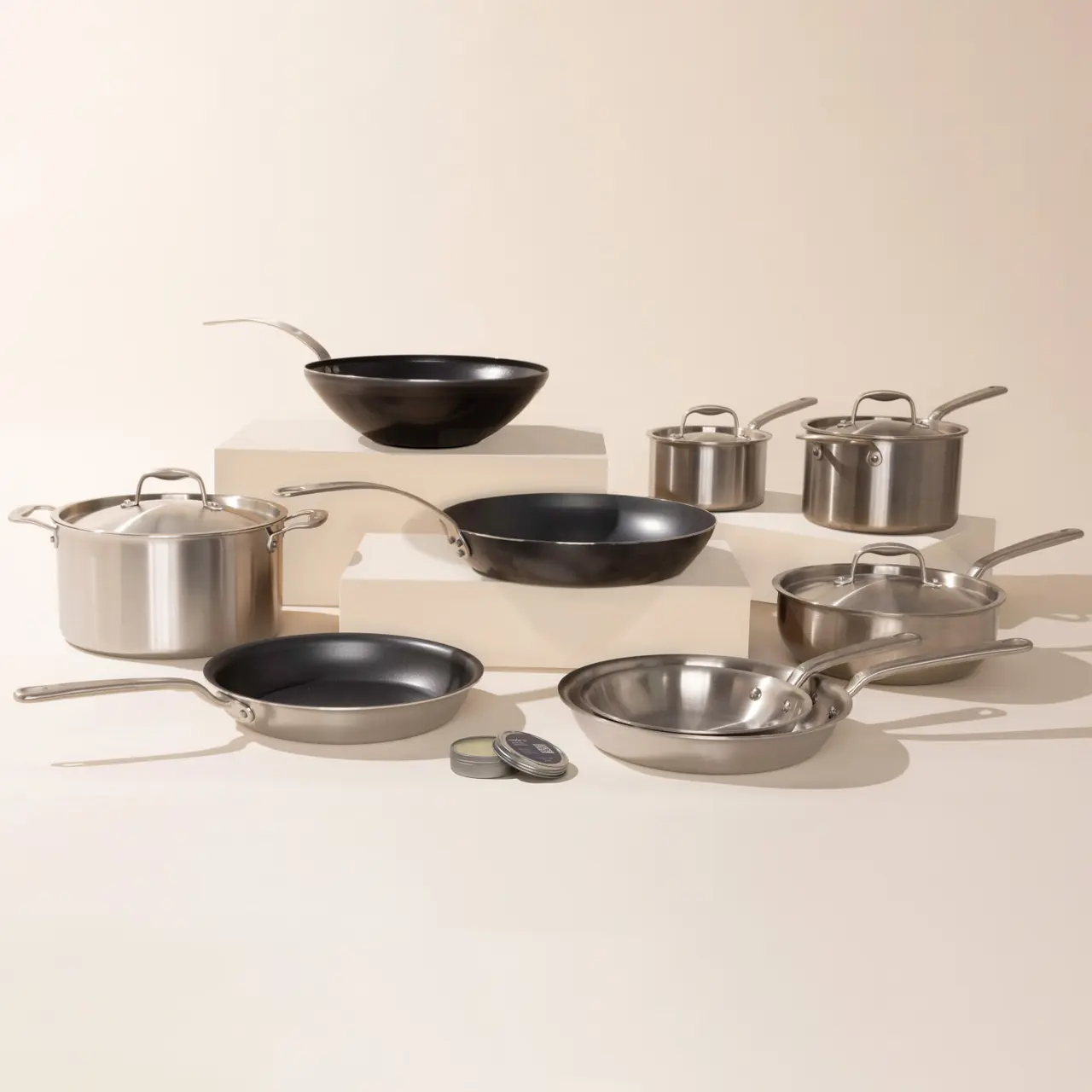 A variety of stainless steel and nonstick pots and pans are neatly arranged on a neutral background, showcasing a cookware set.
