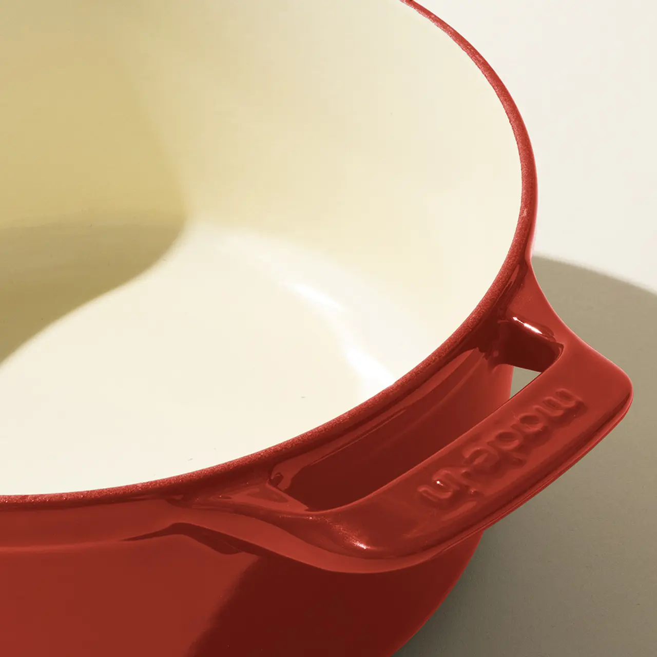 Close-up of a red ceramic baking dish with handles, showcasing its glossy interior and exterior texture.