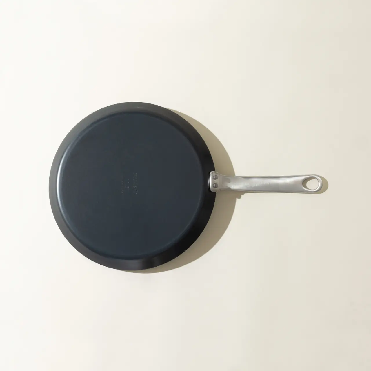 A non-stick frying pan with a long handle is placed on a light-colored surface, viewed from above.