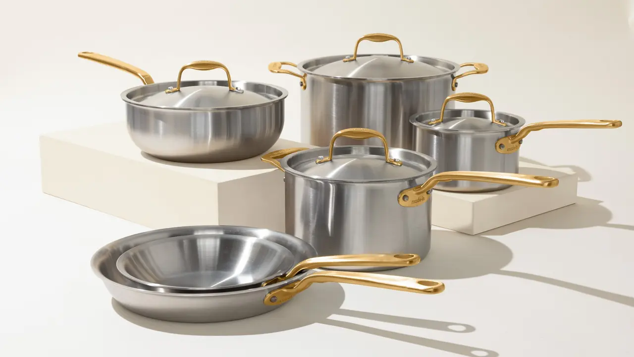 A set of stainless steel cookware with gold-toned handles is arranged elegantly against a neutral background.