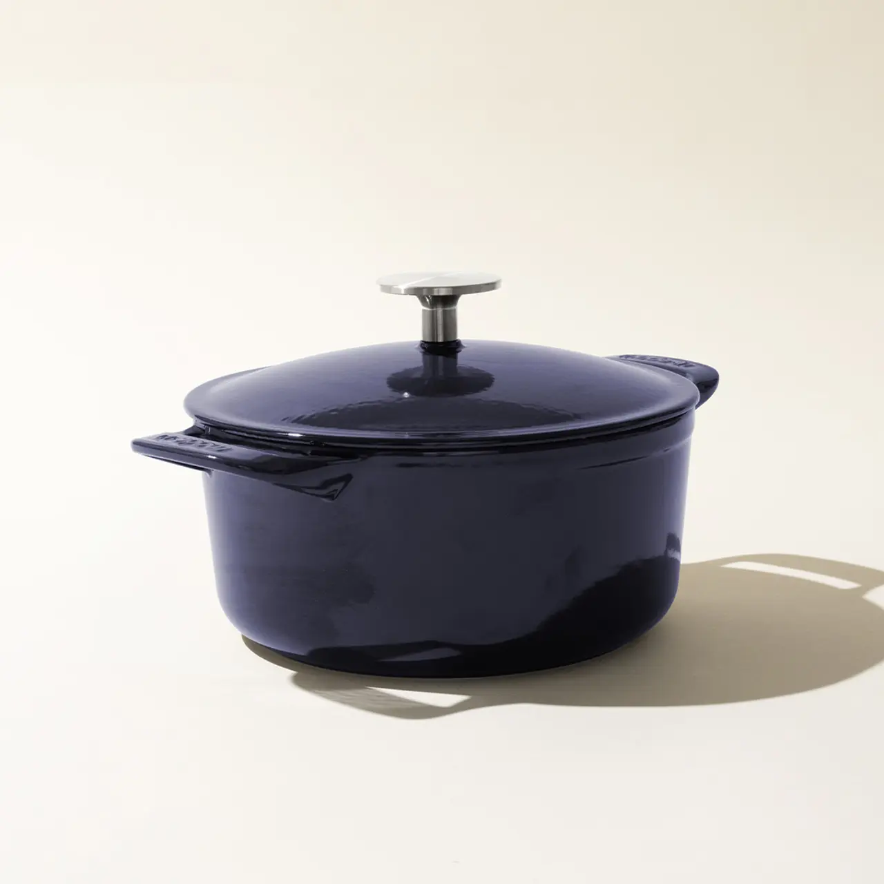 A blue enameled cast iron Dutch oven with the lid on, sitting against a light background with a soft shadow to the right.