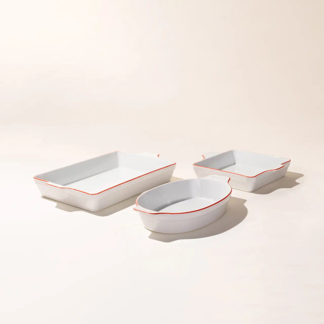 A set of three white ceramic dishes with red trim on a light background.