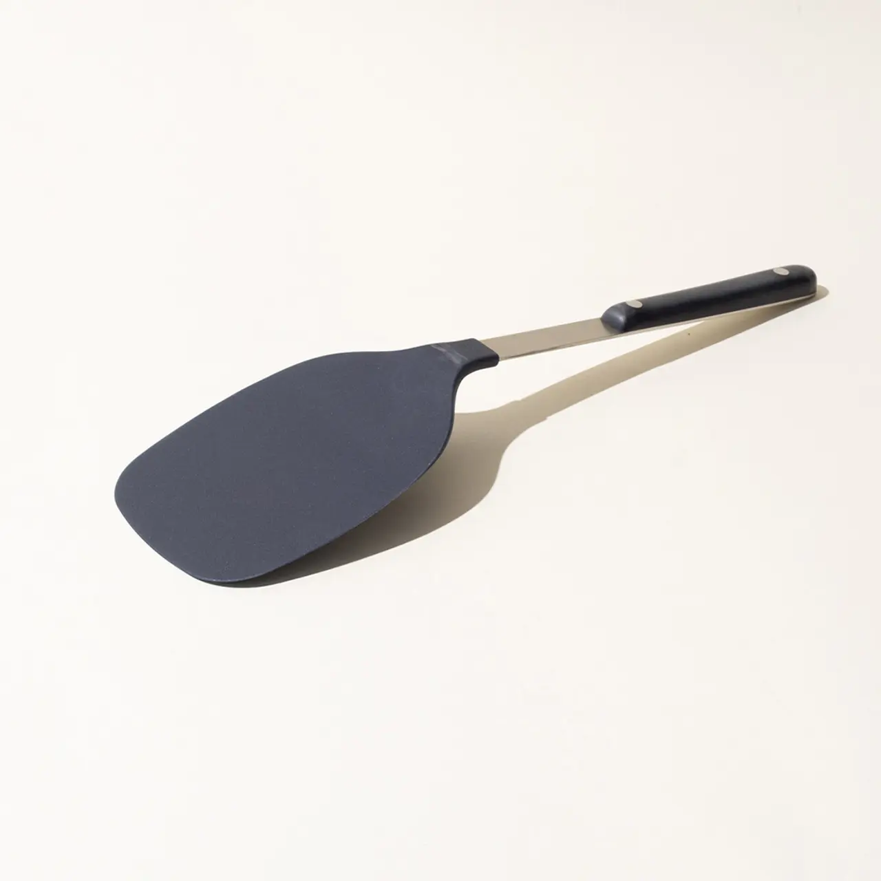 A black silicone spatula with a long handle is lying on a neutral surface at a slight angle to the viewer.