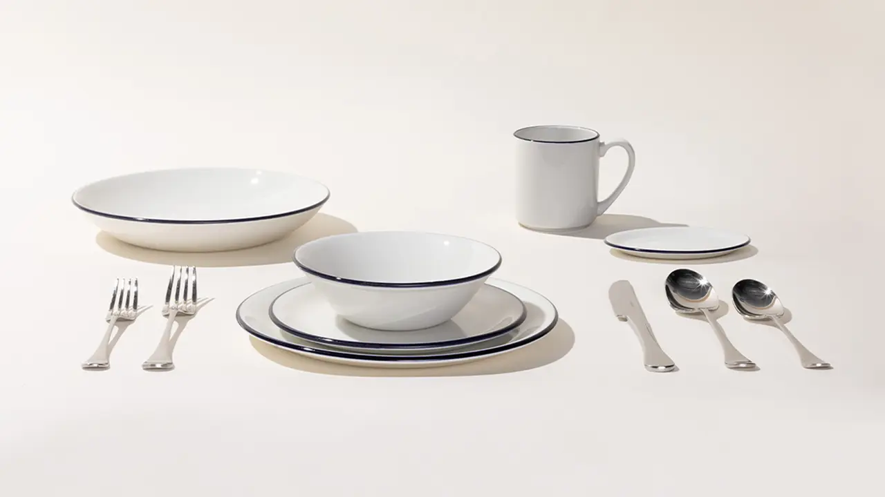 A neatly arranged dinnerware set with plates, bowls, a mug, and silverware on a light background.