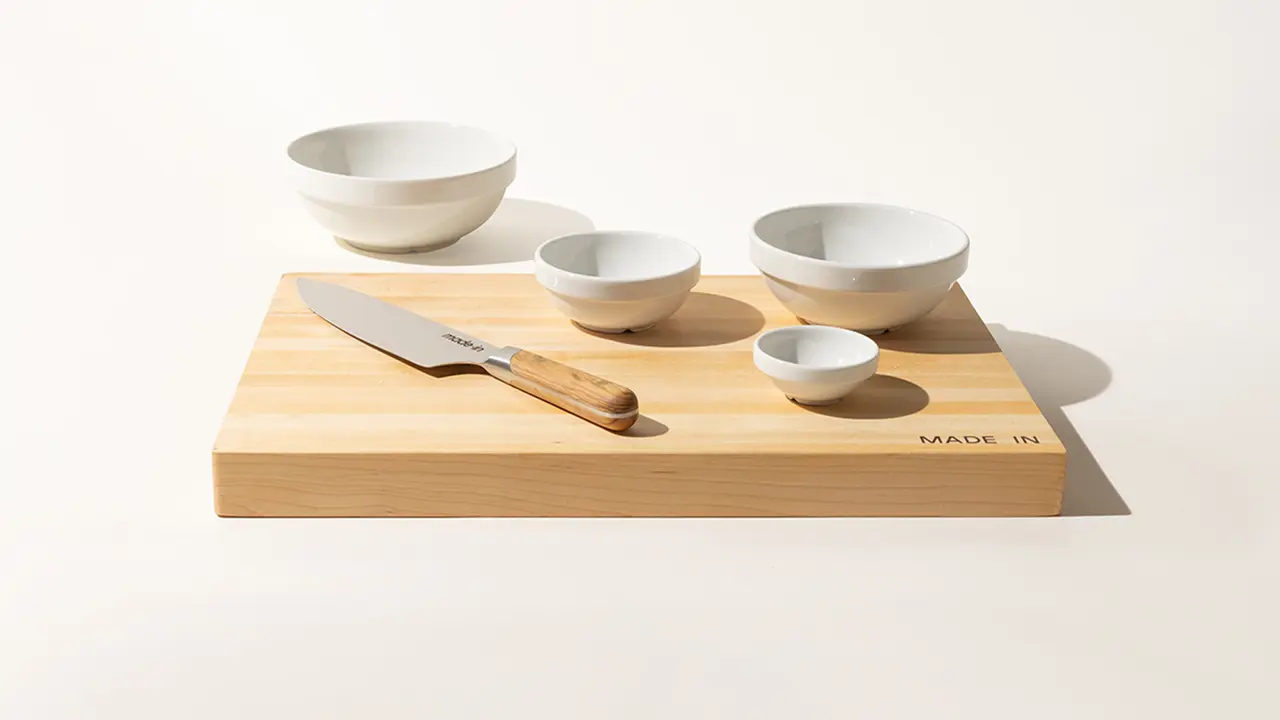 Four white bowls of varying sizes are neatly arranged on a bamboo cutting board with a kitchen knife to the side, all set against a plain background.