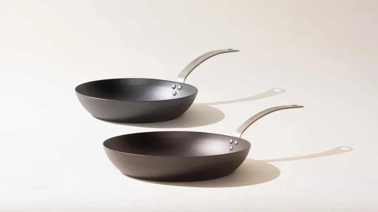 Two black frying pans with silver handles overlapping each other at different angles on a light background.