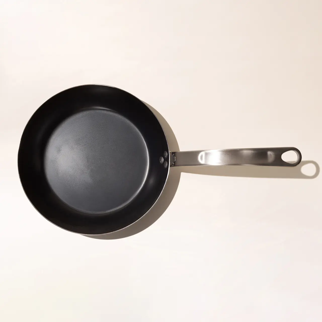 A solitary non-stick frying pan with a stainless steel handle isolated on a light background.