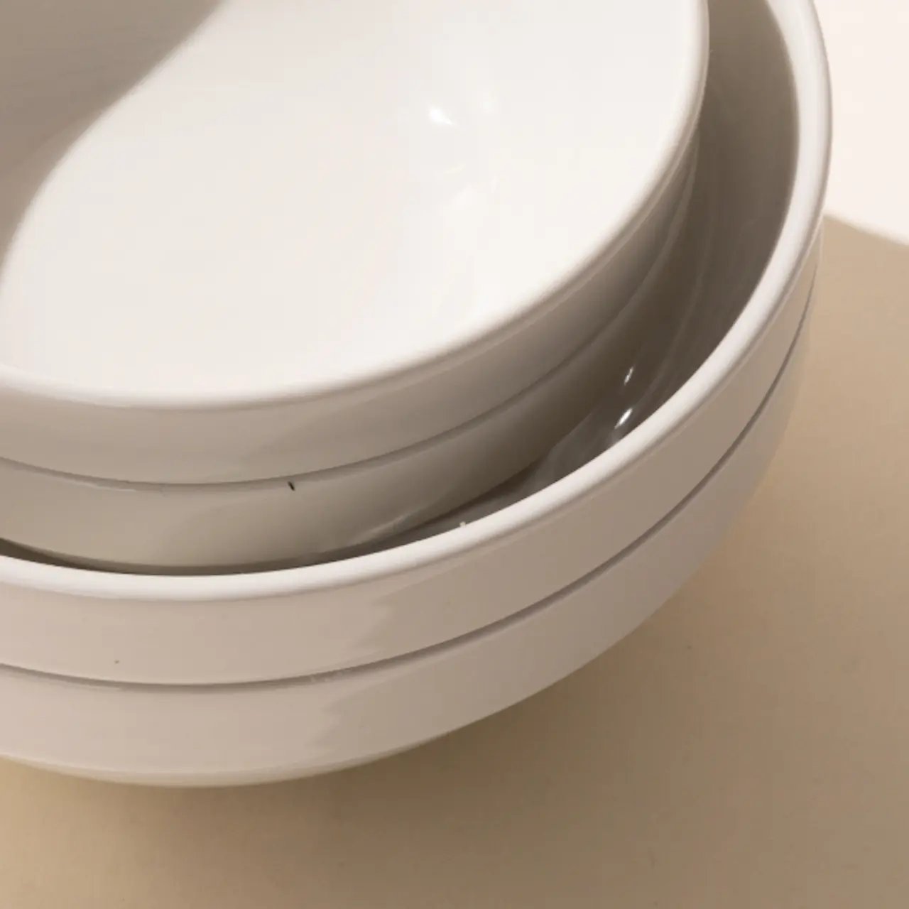 A stack of three white ceramic plates of different sizes placed on a beige surface.