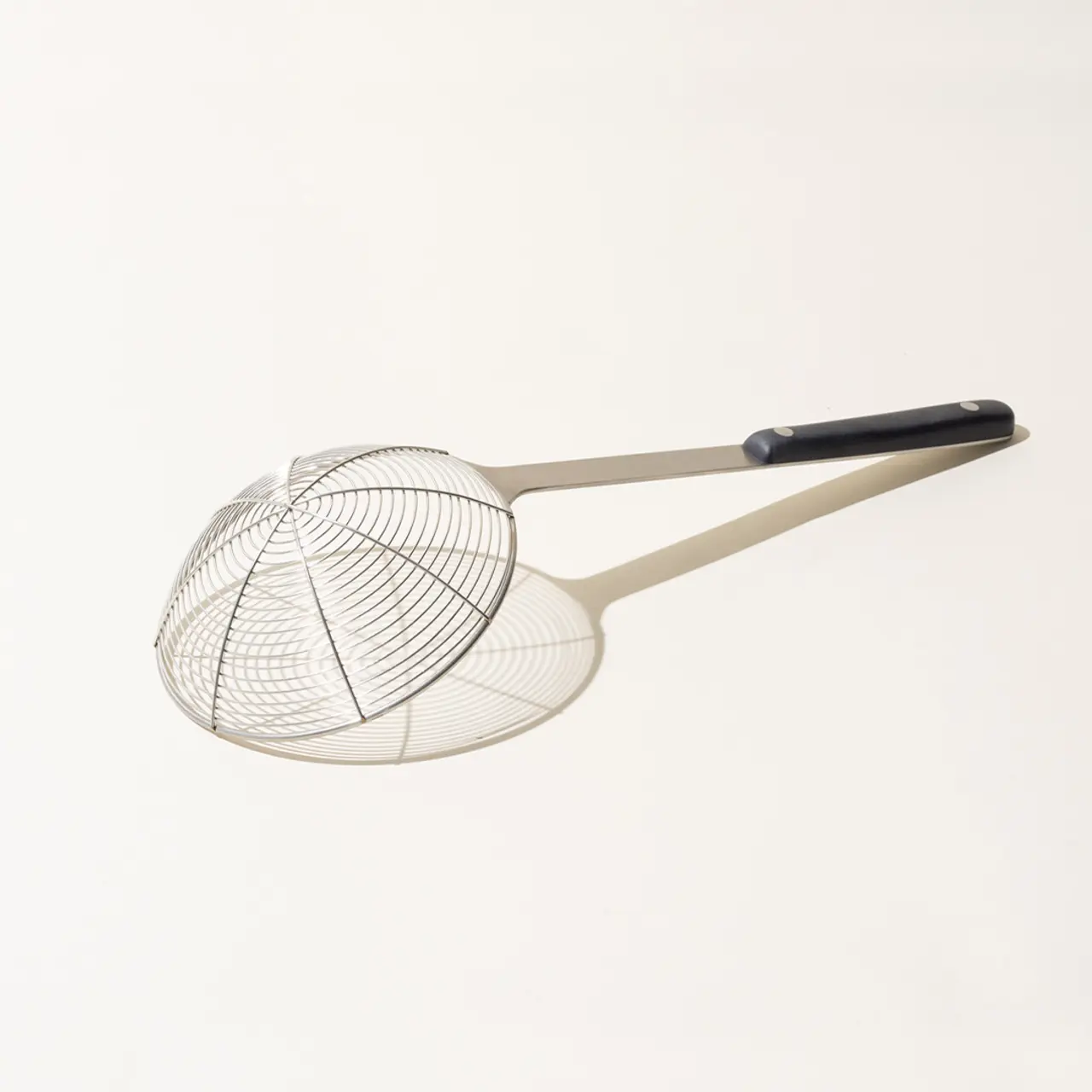 A stainless steel spider strainer with a long handle on a light background.