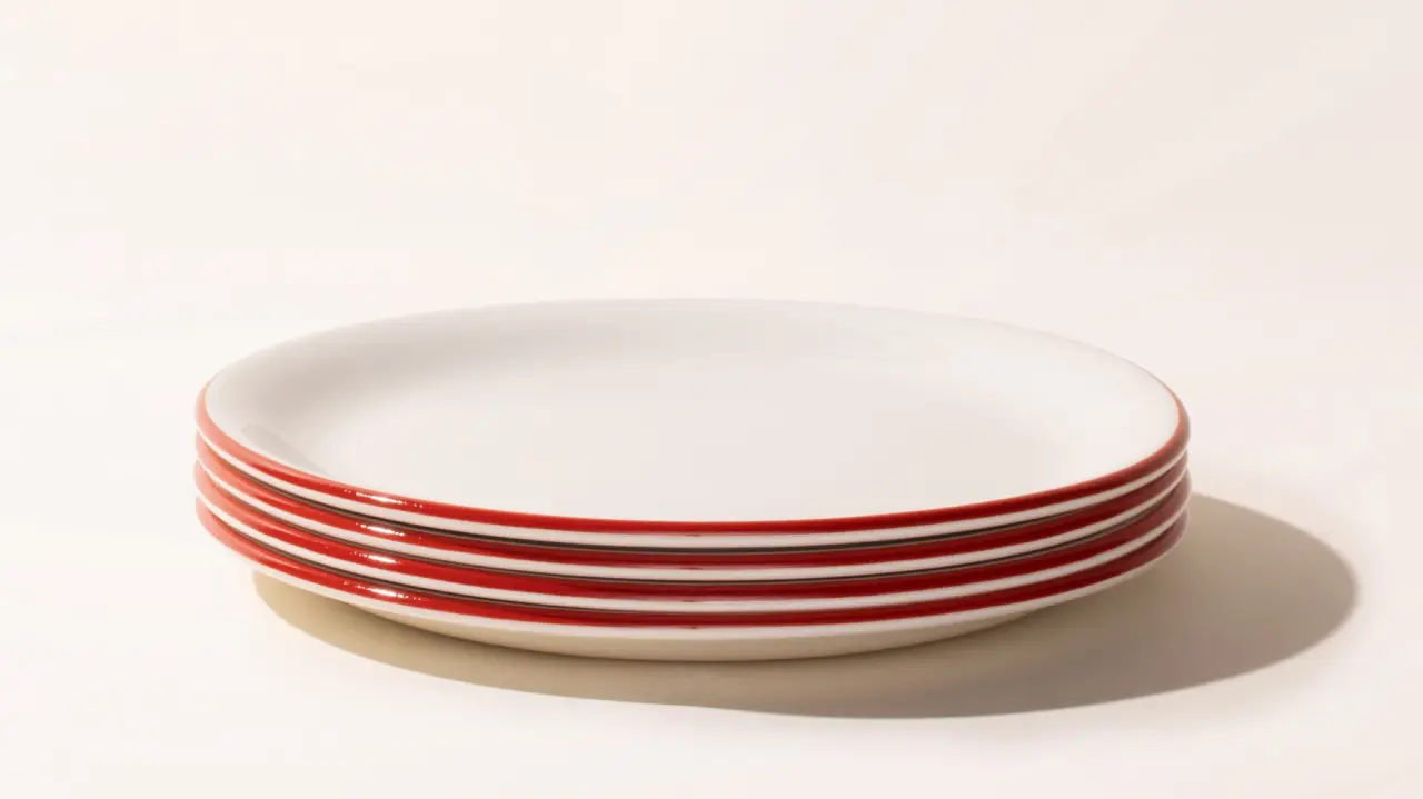 A stack of clean, white plates with a red stripe around the rim on a light background.