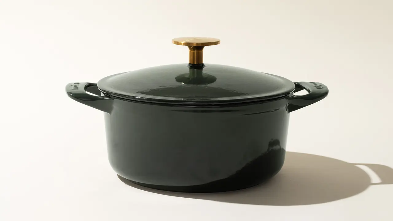 A black pot with a lid and golden knob is placed on a light surface with its shadow visible to the right.