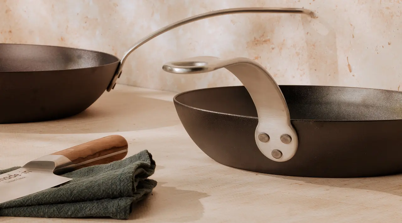 Two non-stick frying pans on a counter with a dark green cloth and a wooden-handled knife nearby.