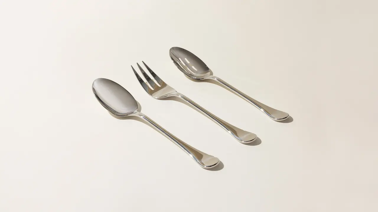 Two spoons and a fork are arranged on a light background, representing common dining utensils.